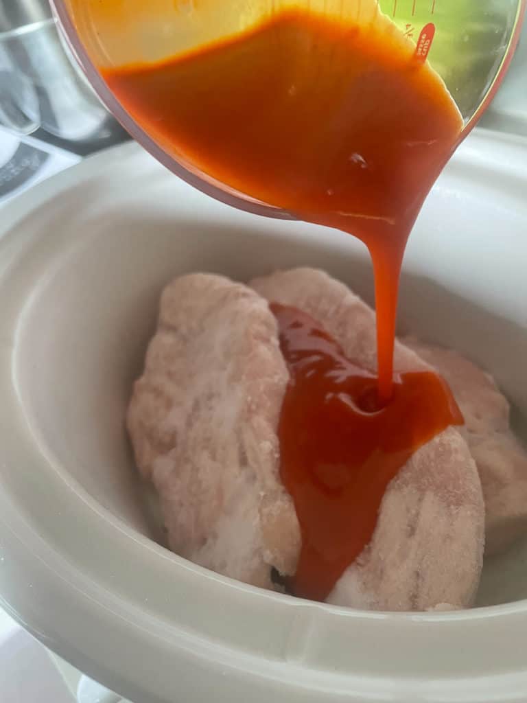 Frank's Red Hot Sauce being poured on chicken in a slow cooker