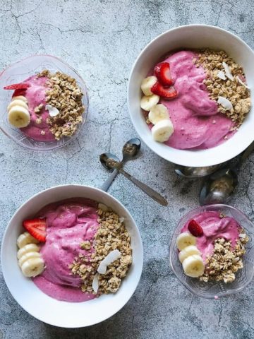 4 bowls of smoothie topped with granola and fruit