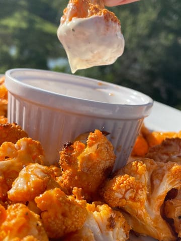 Roasted Cauliflower tossed in buffalo sauce. Picture shows one piece being dipped in ranch