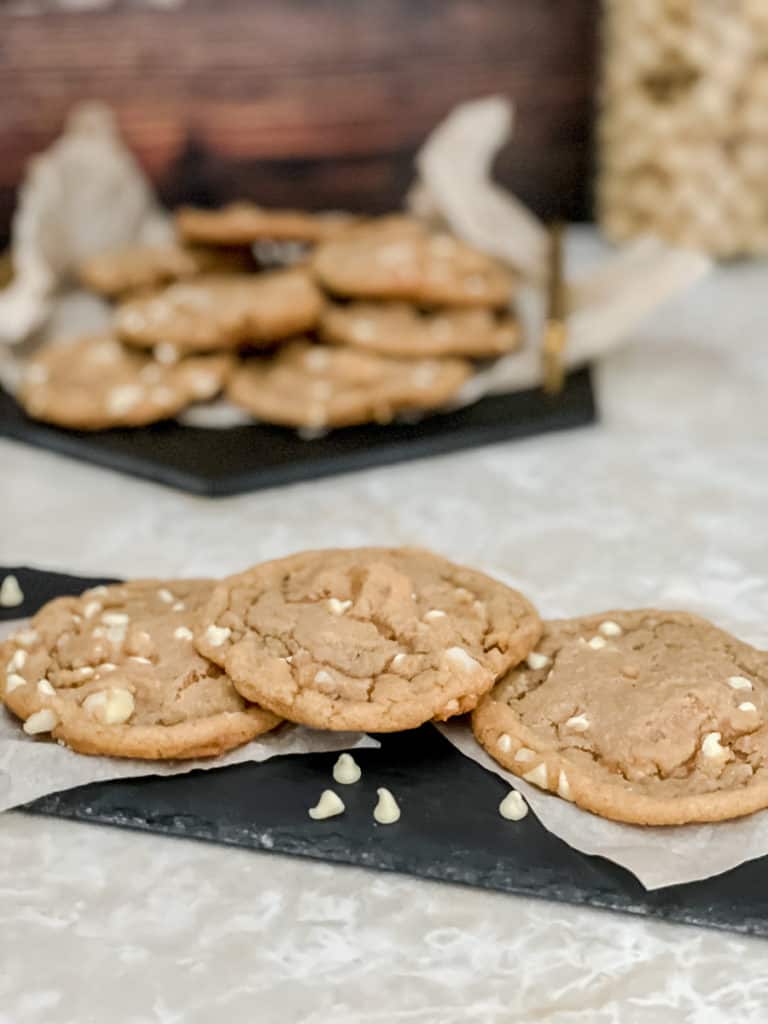 white chocolate macadamia nut cookies sitting on a black plater with parchment underneath