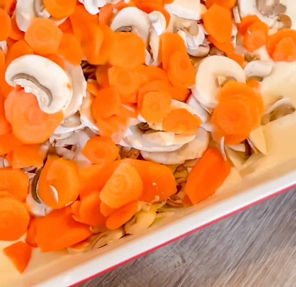 carrots and mushrooms being added to a casserole dish