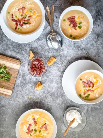 Four Bowls of potato soup with various toppings surrounding them