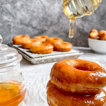 three honey dip donuts stacked on one another with honey dripping on top