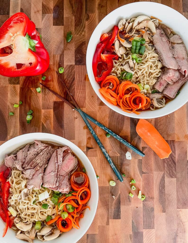 Steak ramen on a wooden cutting board with chopsticks. and vegetables strewn on the board