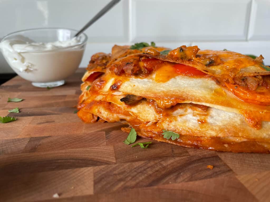 Crispy Tortilla Lasagna on a wooden cutting board with a bowl of sour cream