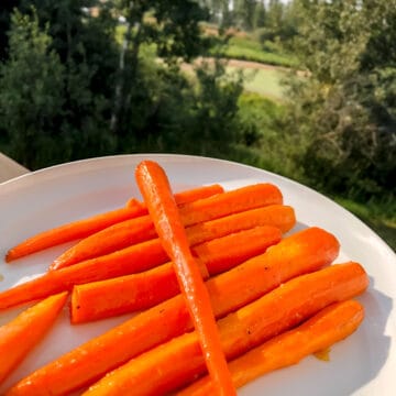 Smoke Carrots with Honey Garlic Glaze on a white platter with trees in the background