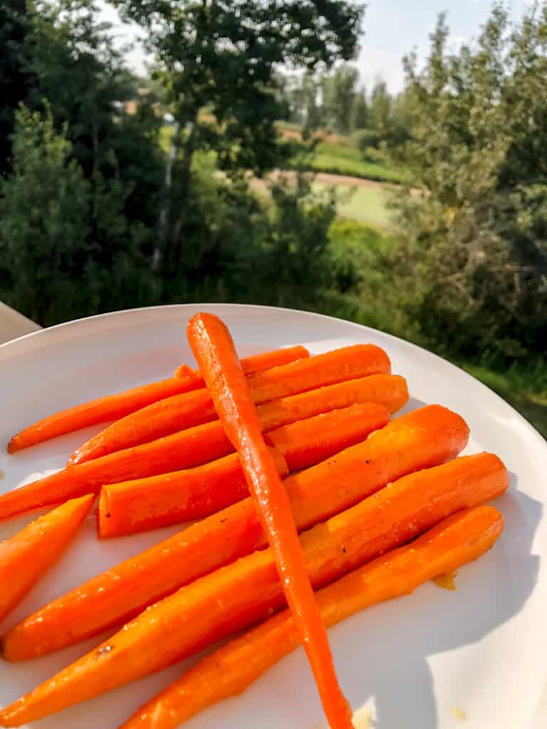Smoked Carrots with a Honey Garlic Glaze on a white platter with trees in the background