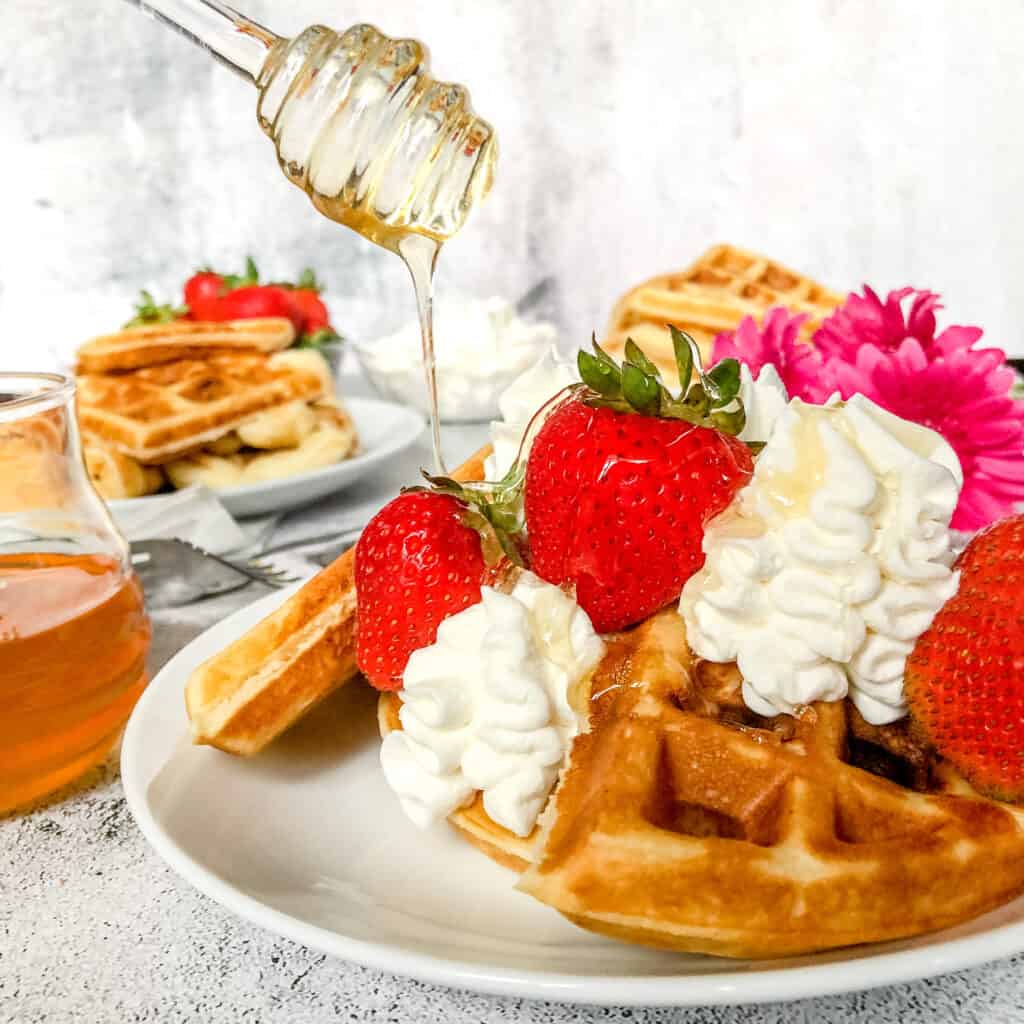Fluffy Waffles with Whiped Cream and Strawberries Drizzled with liquid Honey