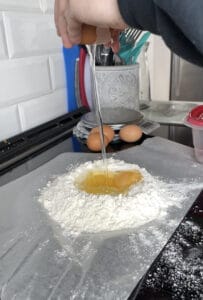 dropping an egg into a well of flour to make traditional fresh pasta