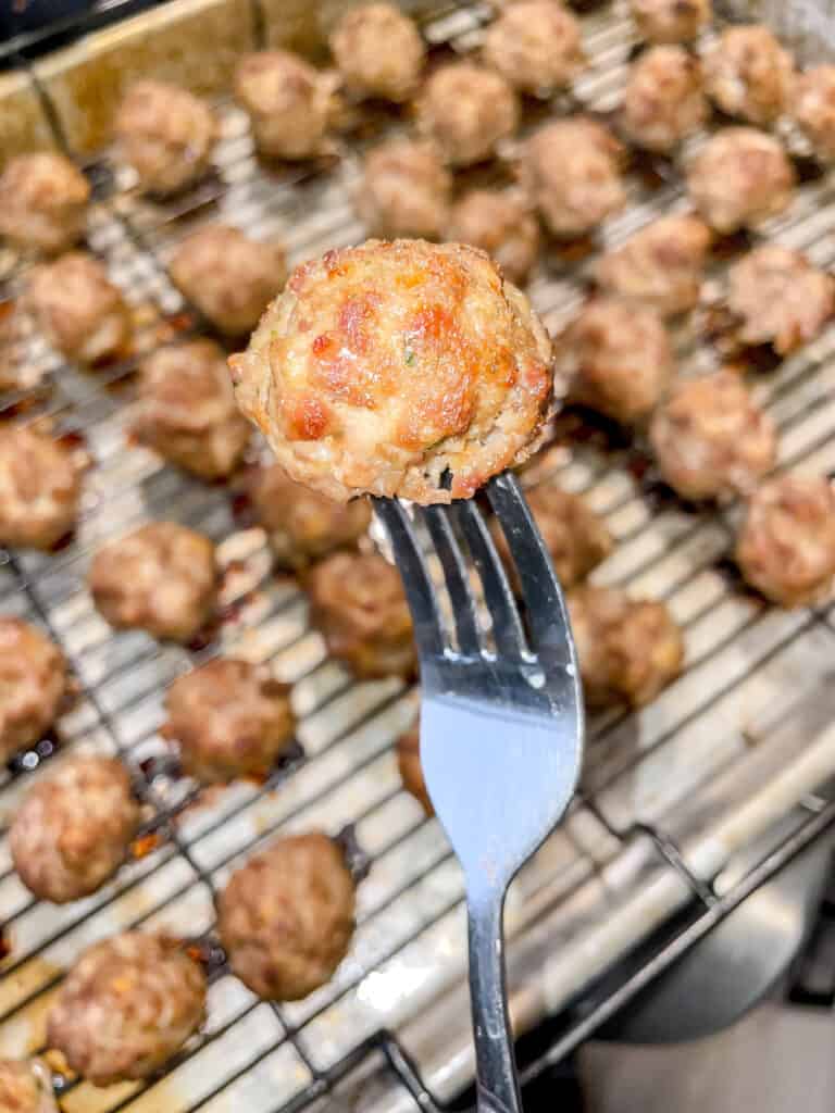 Freezer meatballs on a fork with other meatballs on a rack in the background