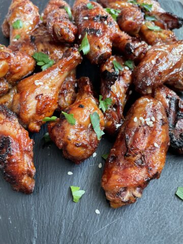 teriyaki chicken wings with parsley and sesame seeds laying on a black slate plate