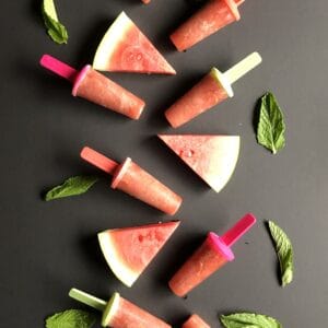 watermelon and mint popsicles on a black background with watermelonf wedges and mint leaves around them