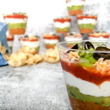 Close up of seven-layer dip cups with more in the background and chips spilled on the table